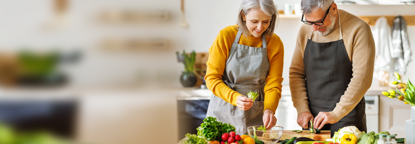 Hombre y mujer con delantales preparan una ensalada en su cocina