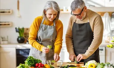Hombre y mujer con delantales preparan una ensalada en su cocina