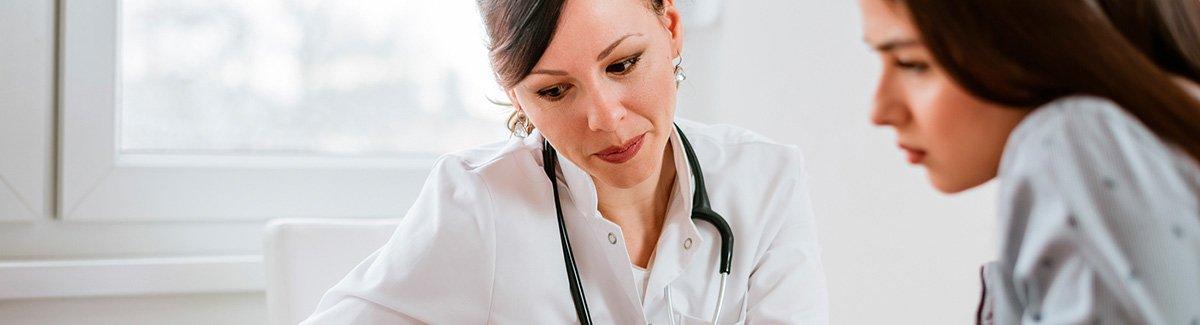 “Médica y paciente en consulta, sentadas revisando un documento”