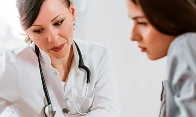 “Médica y paciente en consulta, sentadas revisando un documento”