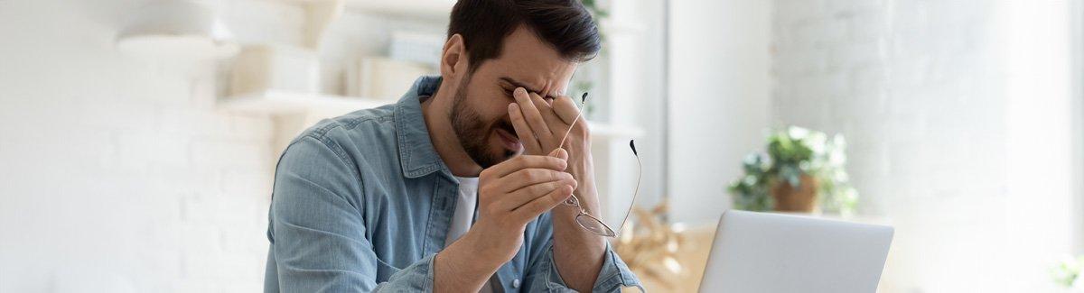 Hombre sosteniendo sus sienes con expresión de dolor, sujetando sus gafas con la otra mano