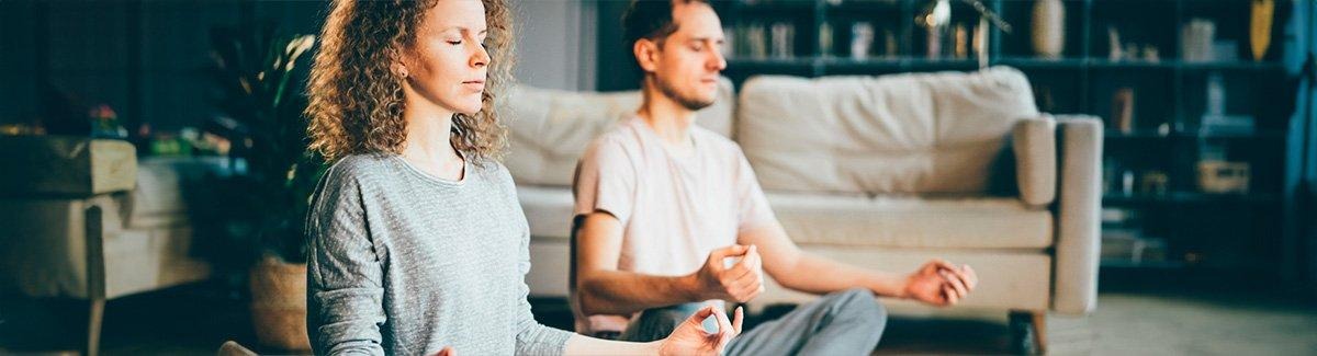 Mujer y hombre meditan sentados con los ojos cerrados en la sala de su casa 