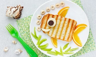 La imágen muestra una comida con forma de pescado formato con un pan tostato y aletas de naranjas