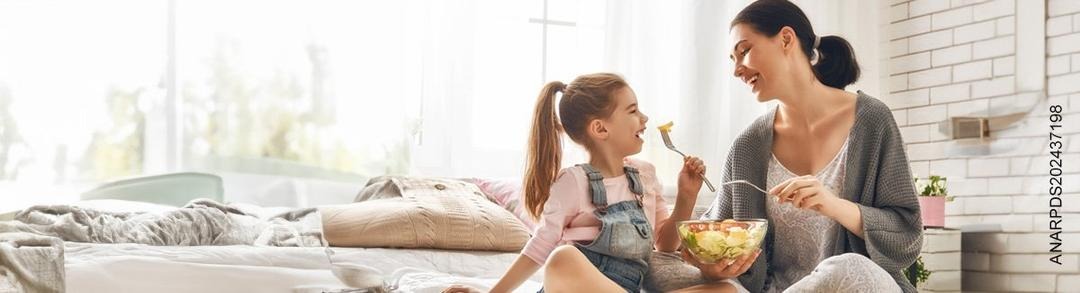 Madre e hija sonríen mientras comen ensalada de un bowl.)