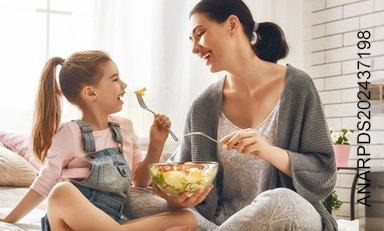 Madre e hija sonríen mientras comen ensalada de un bowl.)