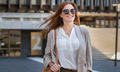 Mujer con gafas de sol camina sonriendo, su pelo se mueve con el viento
