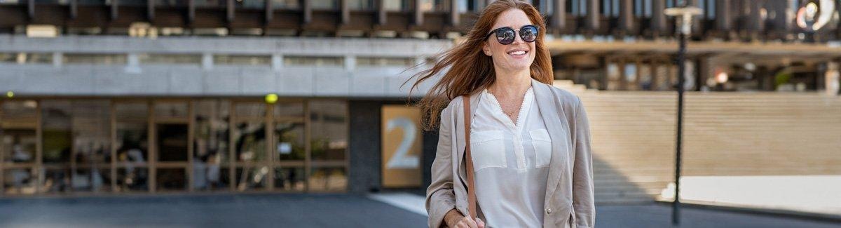 Mujer con gafas de sol camina sonriendo, su pelo se mueve con el viento