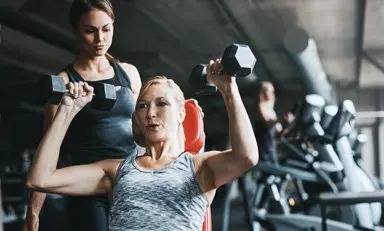 Mujer en gimnasio se ejercita con la supervisión de su entrenadora