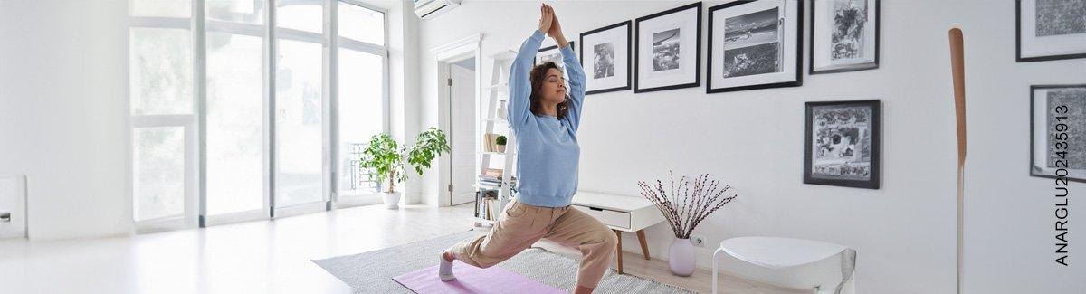 Mujer joven en un apartamento iluminado, ejercitándose, respirando profundamente, transmitiendo salud, equilibrio y serenidad.