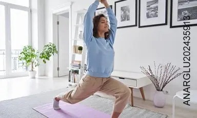 Mujer joven en un apartamento iluminado, ejercitándose, respirando profundamente, transmitiendo salud, equilibrio y serenidad.