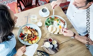 Mujer y hombre desayunan huevos, tostadas y frutas.