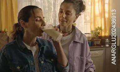 Mujeres en la cocina, una está tomando una bebida y la otra la está observando con gesto de aprobación.