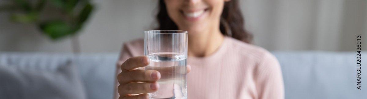 Persona sosteniendo un vaso de agua, sonriendo, evocando a los beneficios de la hidratación en la salud