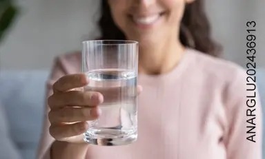 Persona sosteniendo un vaso de agua, sonriendo, evocando a los beneficios de la hidratación en la salud