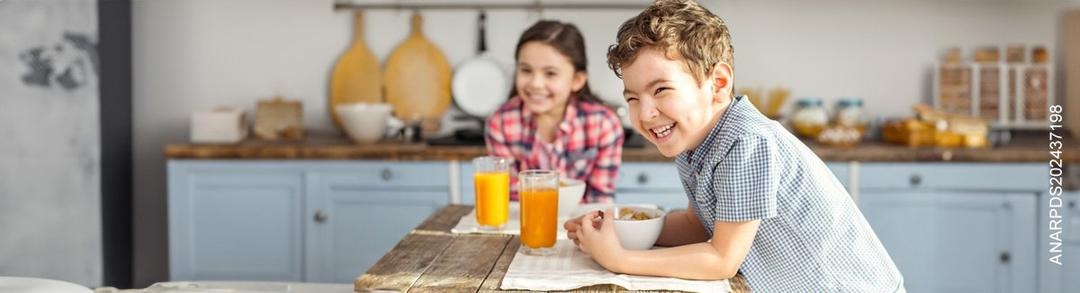 Niños, sentados alrededor de una mesa en la cocina, sonríen.