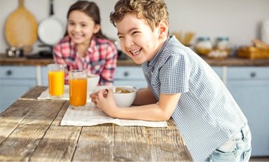 Niños, sentados alrededor de una mesa en la cocina, sonríen.