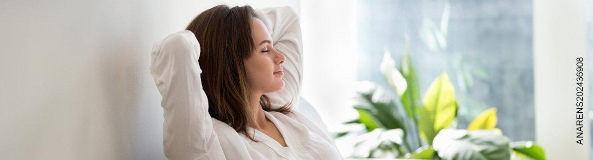 Mujer en casa descansando con los ojos cerrados y los brazos atrás de la cabeza 