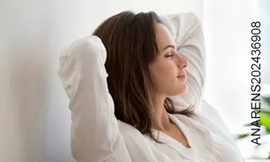 Mujer en casa descansando con los ojos cerrados y los brazos atrás de la cabeza 