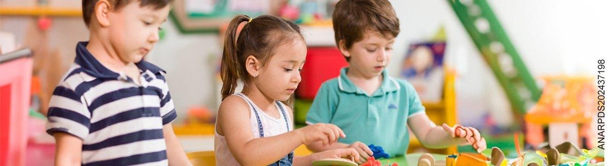 Tres niños juegan de lante de una mesa con juguetes de madera.