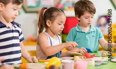 Tres niños juegan de lante de una mesa con juguetes de madera.