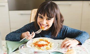 Dos niños sentados en una mesa en una cocina, cada uno bebiendo de un vaso. El niño a la izquierda tiene el cabello largo y sostiene el vaso con ambas manos